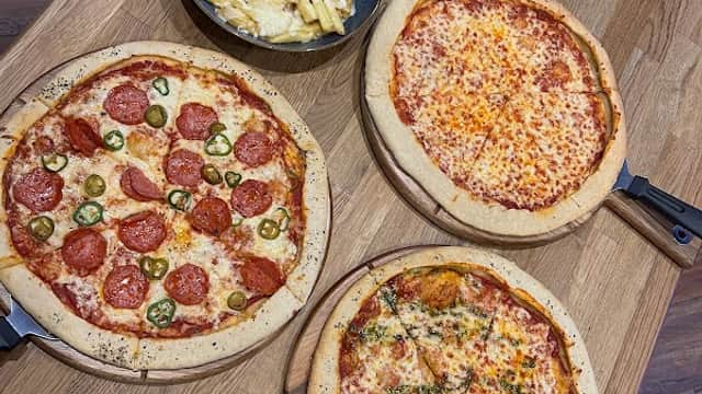Four pizzas on wooden boards with a bowl of fries, set on a wooden table in a cozy bar environment.