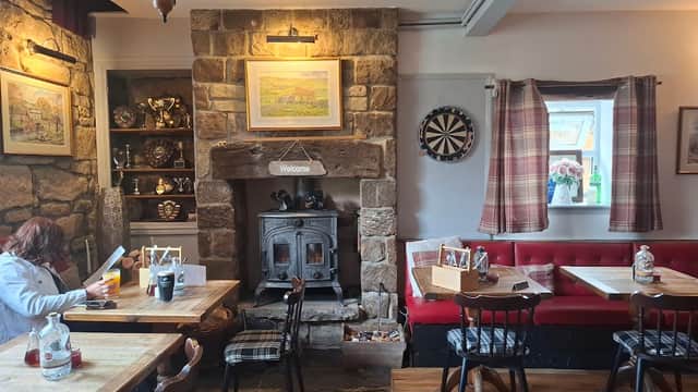Cozy pub interior with stone walls, wooden tables, a dartboard, and a welcoming fireplace. Warm lighting enhances the atmosphere.