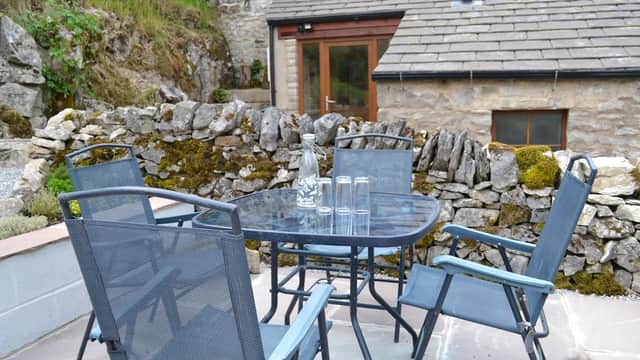 Outdoor seating area with a glass table and chairs, surrounded by stone walls and greenery at Ashes Farm.