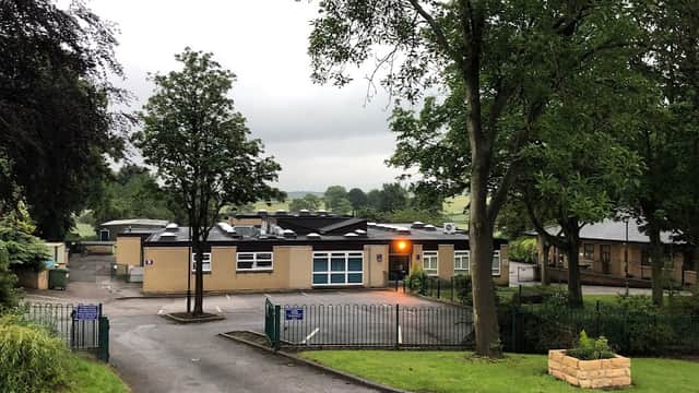 Badsworth C of E Junior & Infant School surrounded by trees, with a parking area and cloudy sky in the background.