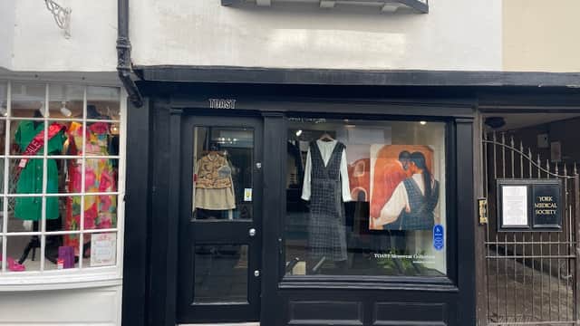 Black storefront of TOAST with clothing displays, including a dress and a patterned top, next to a colorful window display.