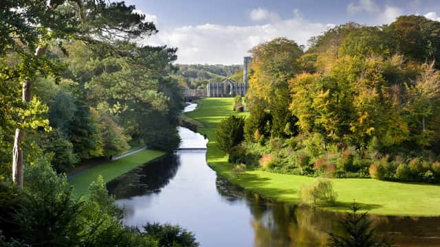 Serene river flanked by lush autumn trees, leading to historic abbey ruins under a clear blue sky.