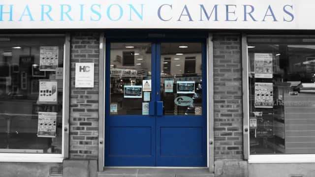Storefront of Harrison Cameras featuring large windows, blue door, and signage in a brick building.
