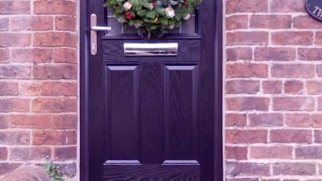 Black front door adorned with a festive wreath, surrounded by brick walls and potted plants on stone steps.