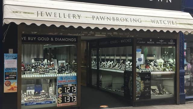 Jewellery shop front featuring displays of watches, gold, and diamonds, with a sign for pawnbroking services.