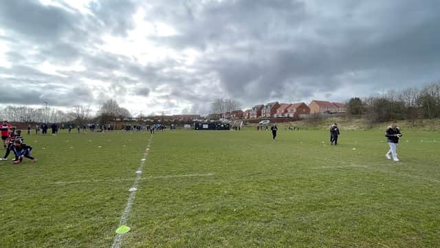Spectators in a grassy field with rugby pitch markings, surrounded by houses under a cloudy sky in Mosborough, Yorkshire.