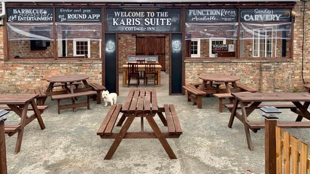 Welcoming entrance of The Cottage Inn with outdoor seating, a white dog, and signage for events and dining.