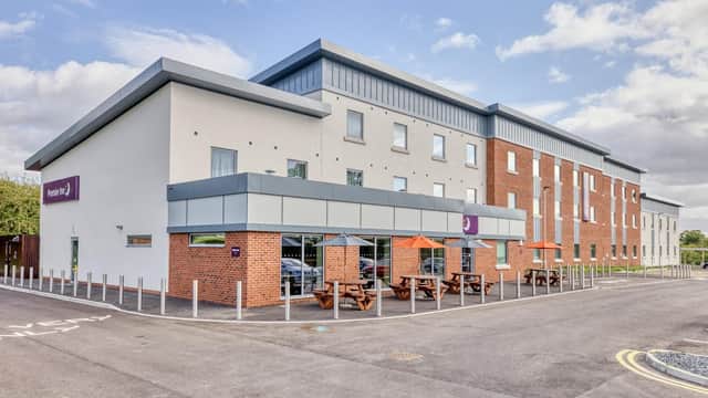 Modern hotel building with a mix of brick and white exterior, outdoor seating with orange umbrellas, and clear blue sky.