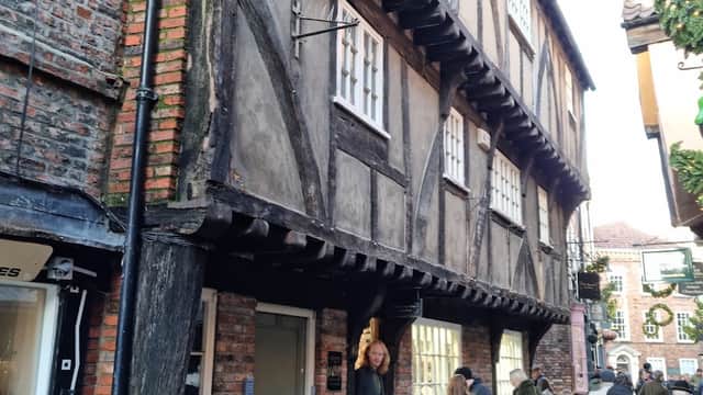 Historic timber-framed building with shopfront, people walking by, and festive decorations in York's Shambles area.