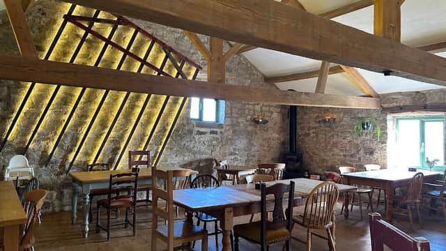 Rustic restaurant interior with wooden beams, stone walls, and empty tables surrounded by chairs in a cozy atmosphere.