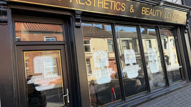 Signage for "The Aesthetics & Beauty Lounge" on a black storefront with large windows and decorative elements.