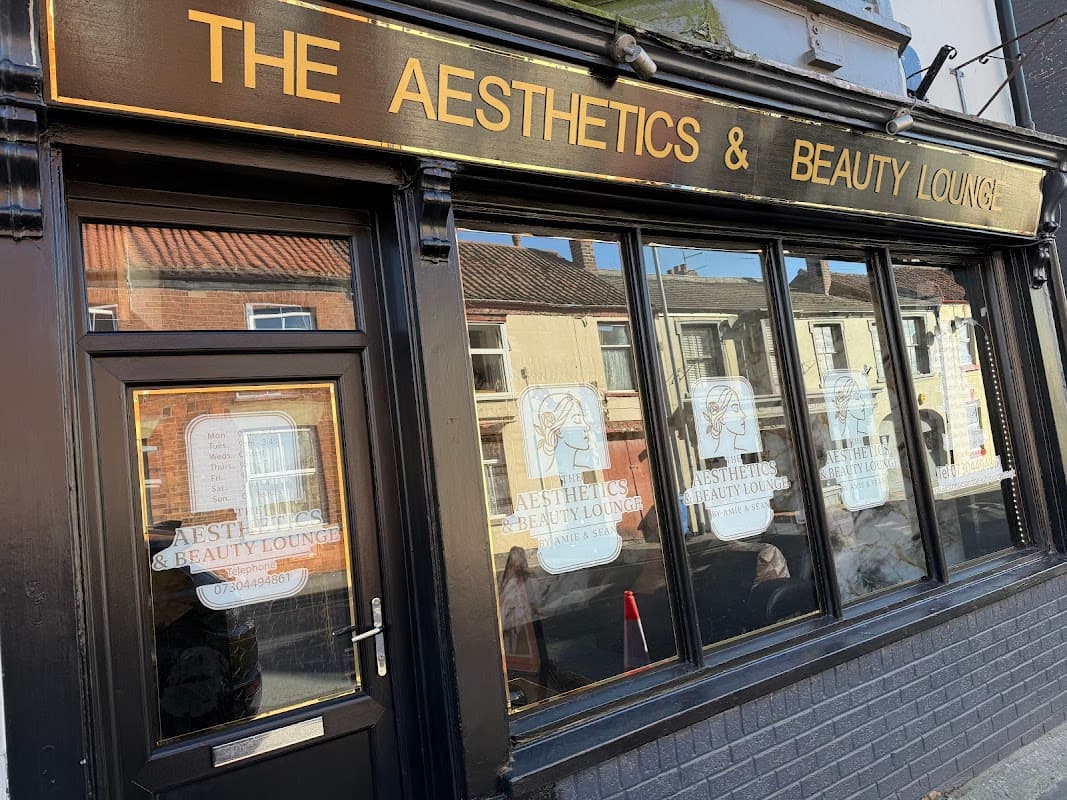 Signage for "The Aesthetics & Beauty Lounge" on a black storefront with large windows and decorative elements.