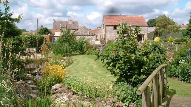 Lush garden with flowers, stone cottages, and a wooden bridge under a cloudy sky in Newton-upon-Rawcliffe, Yorkshire.