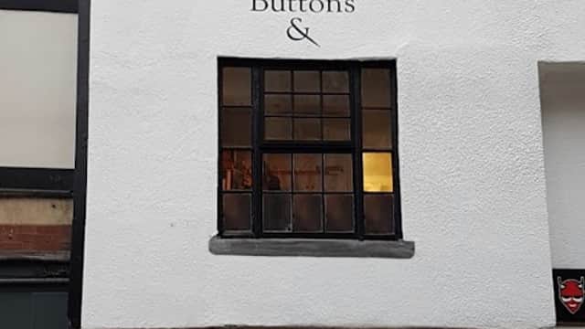 Hobby shop exterior with "Duttons For Buttons" sign, large window displaying craft supplies, and festive decorations.