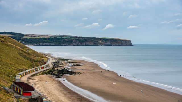 Colorful beach huts line the sandy shore, with gentle waves lapping at the beach and cliffs in the background.