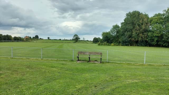 A grassy field with a wooden bench in front of a fence, under a cloudy sky in Brompton, Yorkshire.