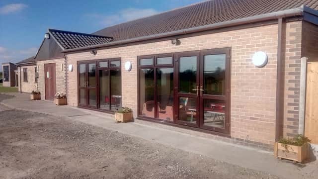 Eastrington Village Hall features large windows, a brick facade, and planters along the entrance against a clear blue sky.