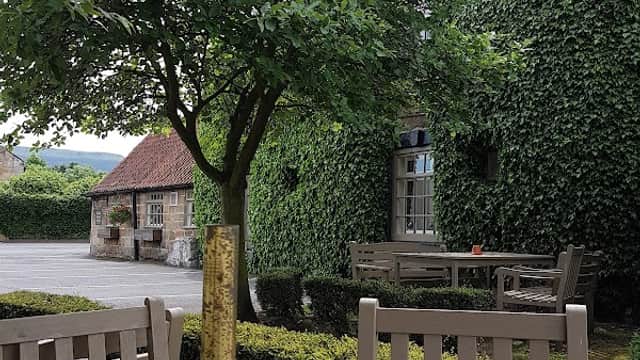 Outdoor dining area with wooden tables, lush greenery, and a view of a stone building in Great Broughton.