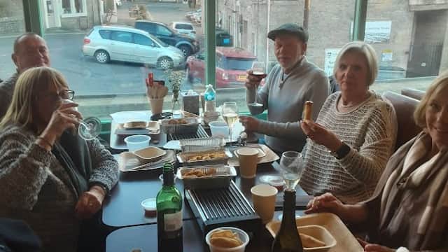 Group of diners enjoying a meal at Darlings of Settle, with drinks and food on the table, in a cozy restaurant setting.