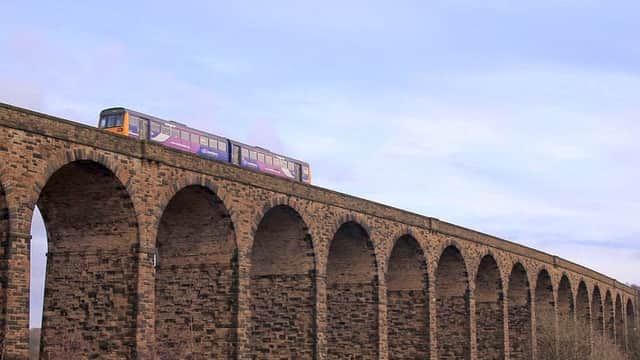 Historic stone viaduct with arches, featuring a train passing overhead against a blue sky.