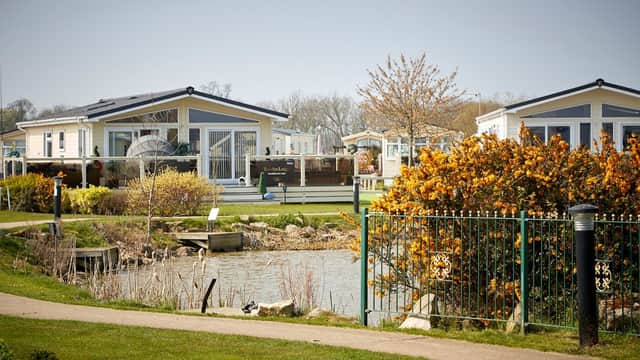 Colorful holiday lodges by a serene pond, surrounded by greenery and blooming flowers at Patrington Haven Leisure Park.