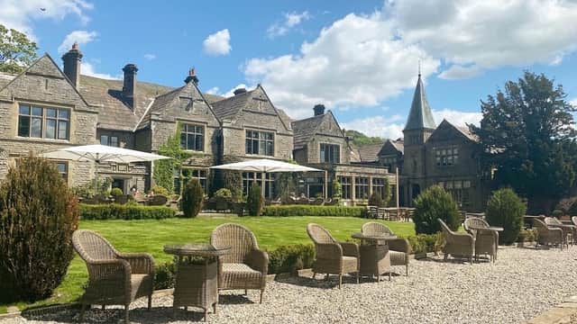 Stone building with a turret, outdoor seating, and lush green lawn under a blue sky with fluffy clouds.