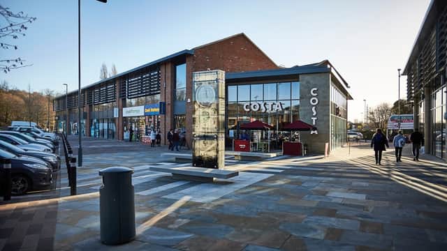 Kirkstall Bridge Shopping Park featuring a Costa café, shops, and parked cars under clear blue skies.