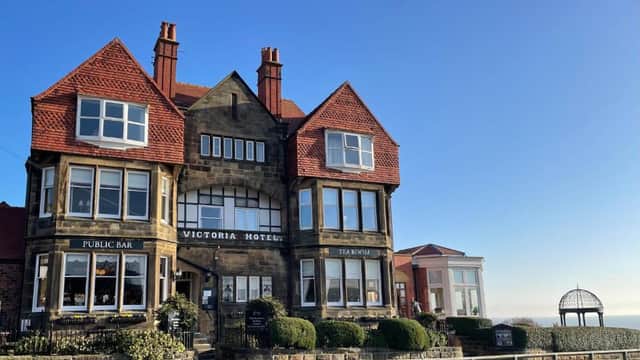 Victorian hotel with red gabled roofs, large windows, and manicured shrubs under a clear blue sky.