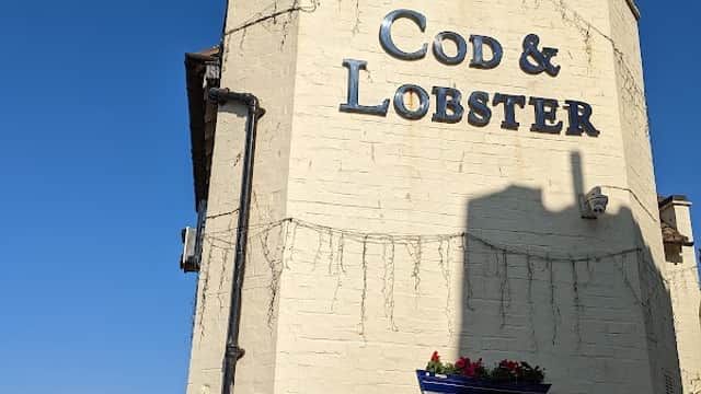 Exterior of Cod & Lobster pub with signage, a red vehicle, and a view of the sea in Hinderwell, Yorkshire.