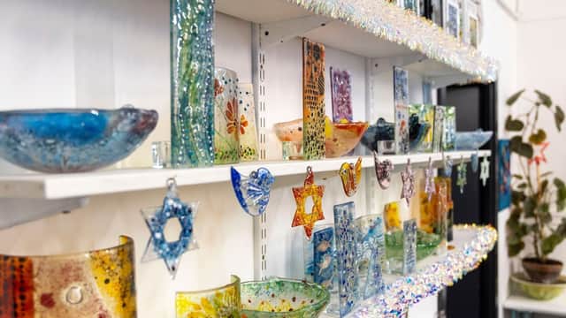 Colorful glass crafts displayed on shelves, featuring bowls, stars, and decorative pieces in a bright, inviting setting.