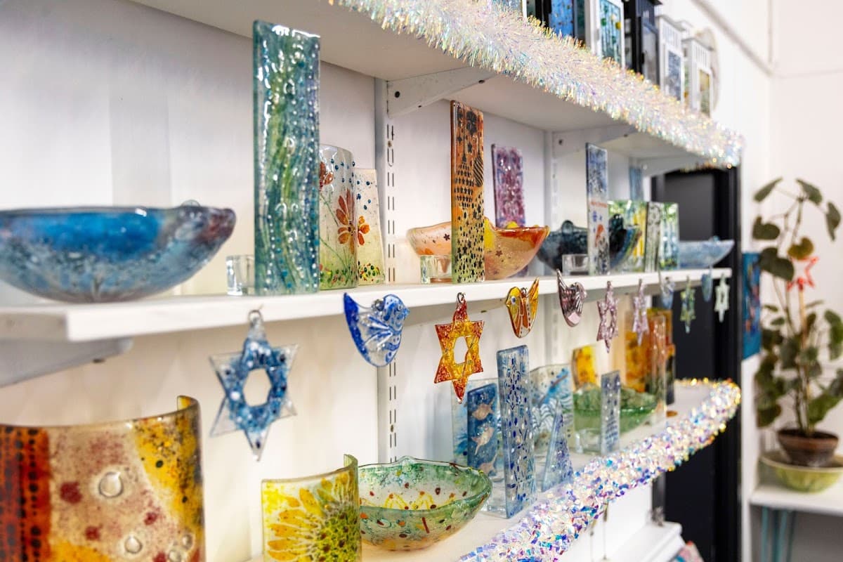 Colorful glass crafts displayed on shelves, featuring bowls, stars, and decorative pieces in a bright, inviting setting.