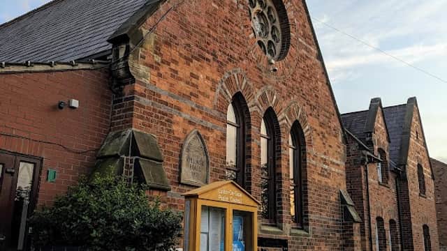 Brick building with arched windows, a decorative rose window, and benches outside in Linton-on-Ouse, Yorkshire.