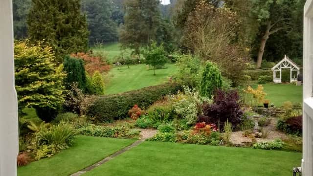 Lush garden with colorful plants and trees, leading to a serene landscape in Lastingham, Yorkshire.