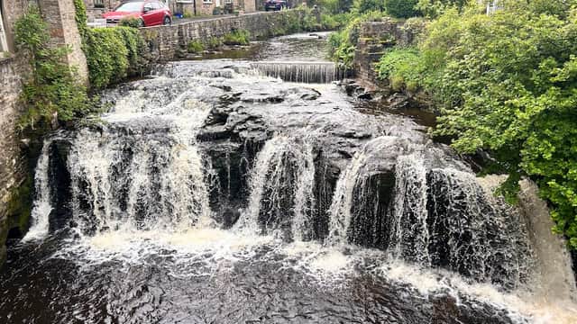 A picturesque cottage by a flowing stream with small waterfalls, surrounded by lush greenery in Sedbusk, Yorkshire.