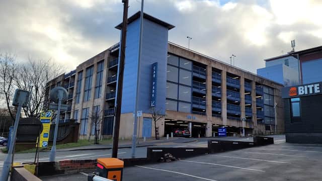 Multi-storey car park with blue and grey exterior, adjacent to a burger restaurant and parking barriers.
