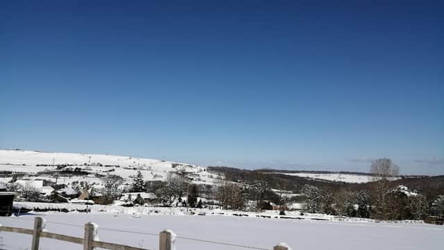 Snow-covered landscape with hills, trees, and a clear blue sky surrounding Deepcar Village Hall.