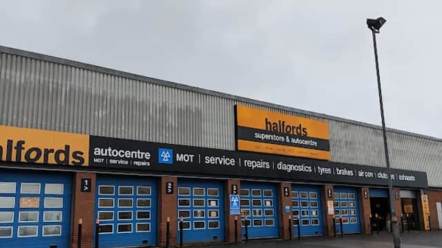Halfords store exterior with blue garage doors, signage for services, and a cloudy sky above.