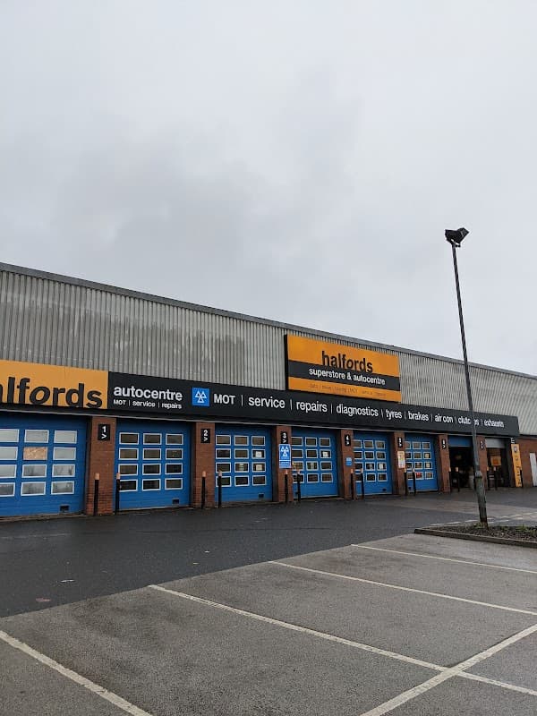 Halfords store exterior with blue garage doors, signage for services, and a cloudy sky above.