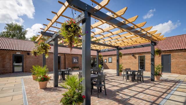 Outdoor cafe area with a wooden pergola, potted plants, and tables under a blue sky at High Farm Holiday Park.