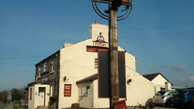 Sign for "The New Inn" bar with a white building and blue sky in Eccup, Yorkshire, featuring a grassy path.