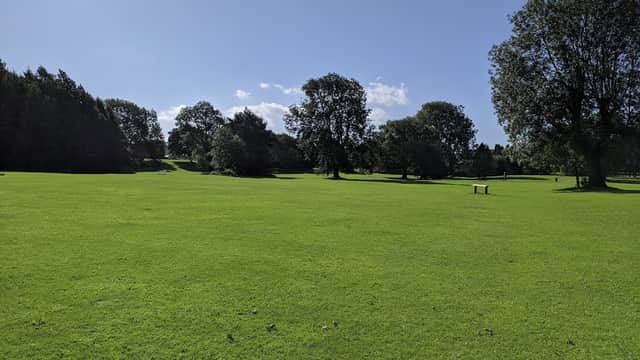 Lush green grass stretches across Nunroyd Park, dotted with trees under a bright blue sky.