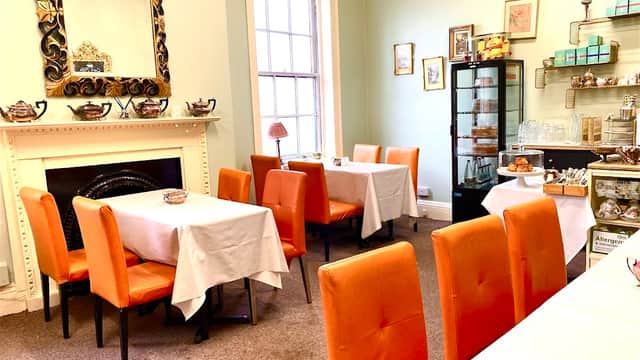 Cozy café with orange chairs, white tablecloths, a decorative mirror, and a display case of pastries.