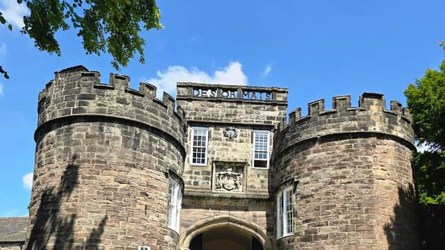 Historic Skipton Castle features stone walls, turrets, and a grand entrance under a bright blue sky.