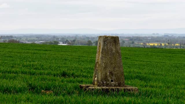 Trig point in a green field with distant hills and a cloudy sky in Moulton, North Yorkshire.