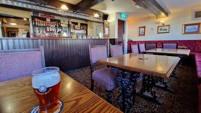 Cozy bar interior with wooden tables, chairs, a counter with drinks, and a pint of beer on a table.