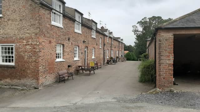 Brick cottages line a gravel path, with benches and greenery in a tranquil rural setting in North Dalton, Yorkshire.