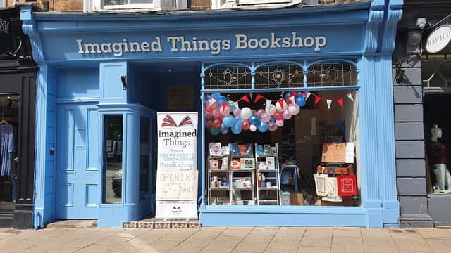 Bright blue storefront with "Imagined Things Bookshop" sign, colorful balloons, bunting, and a display of books.