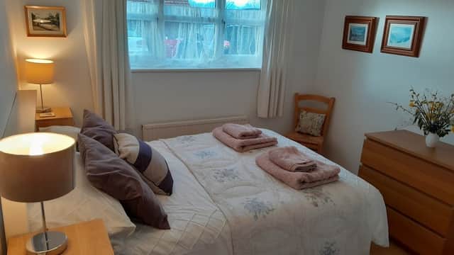 Cozy bedroom with a double bed, decorative pillows, wooden furniture, and soft lighting, featuring a window view.