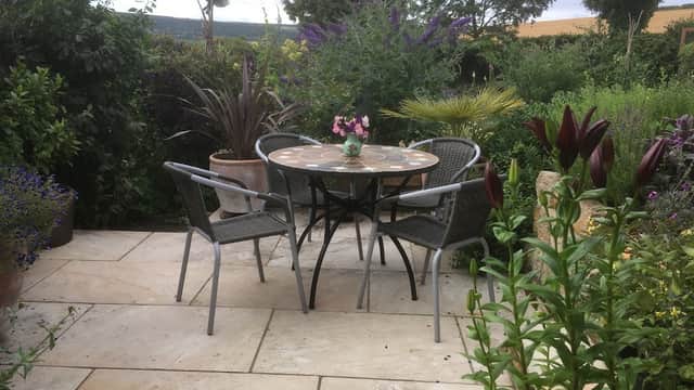 Charming outdoor seating area with a round table and chairs surrounded by lush greenery and colorful flowers.