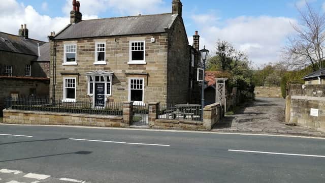 Stone hotel with a fenced front yard, large windows, and a driveway, set against a blue sky in Yorkshire.